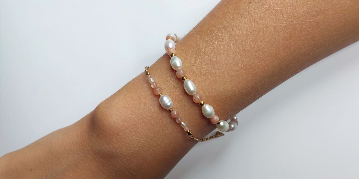 Vue d'un bras portant deux styles de bracelets différents avec des perles d'eau douce blanches et des pierres naturelles en pierre de soleil sur un fond blanc.