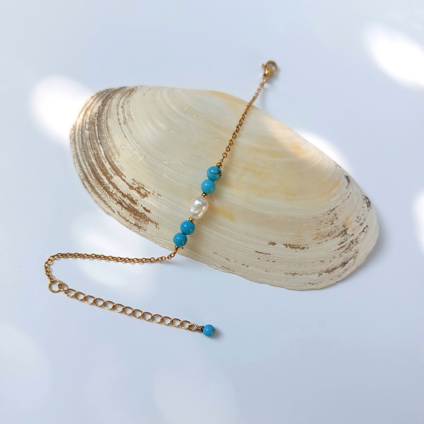 Bracelet élégant Acropora en perle d'eau douce et perles de turquoise bleu posé sur fond gris.