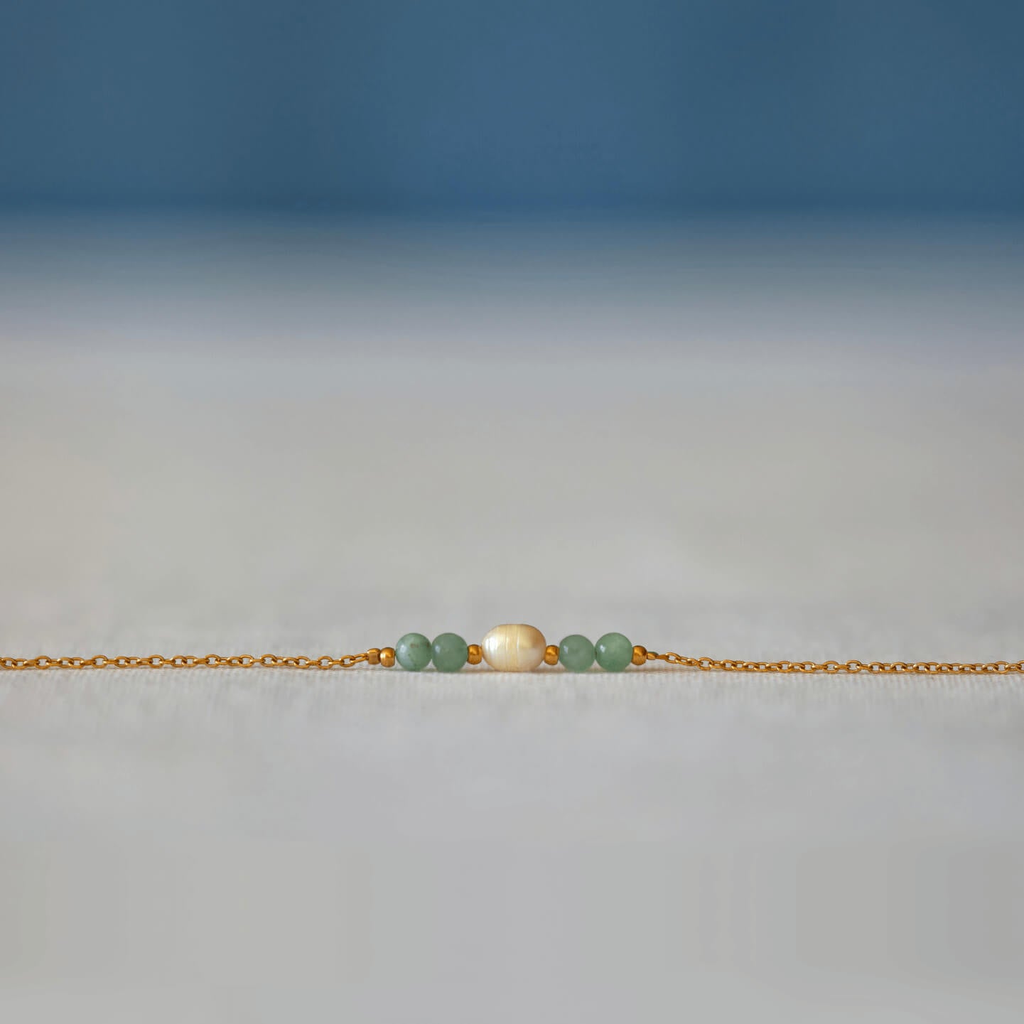 Bracelet élégant Acropora en perle d'eau douce et perles d'aventurine verte posé sur fond gris.