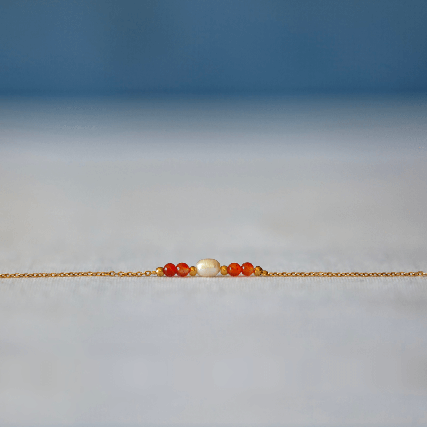 Bracelet élégant Acropora en perle d'eau douce et perles de cornaline orange posé sur fond gris.