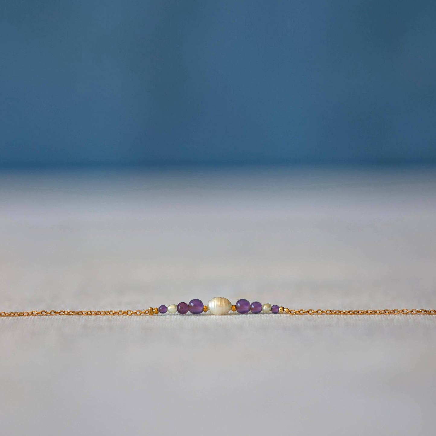Bracelet Anthelia en perles d'eau douce et perles d'Améthyste violette posé sur fond gris.