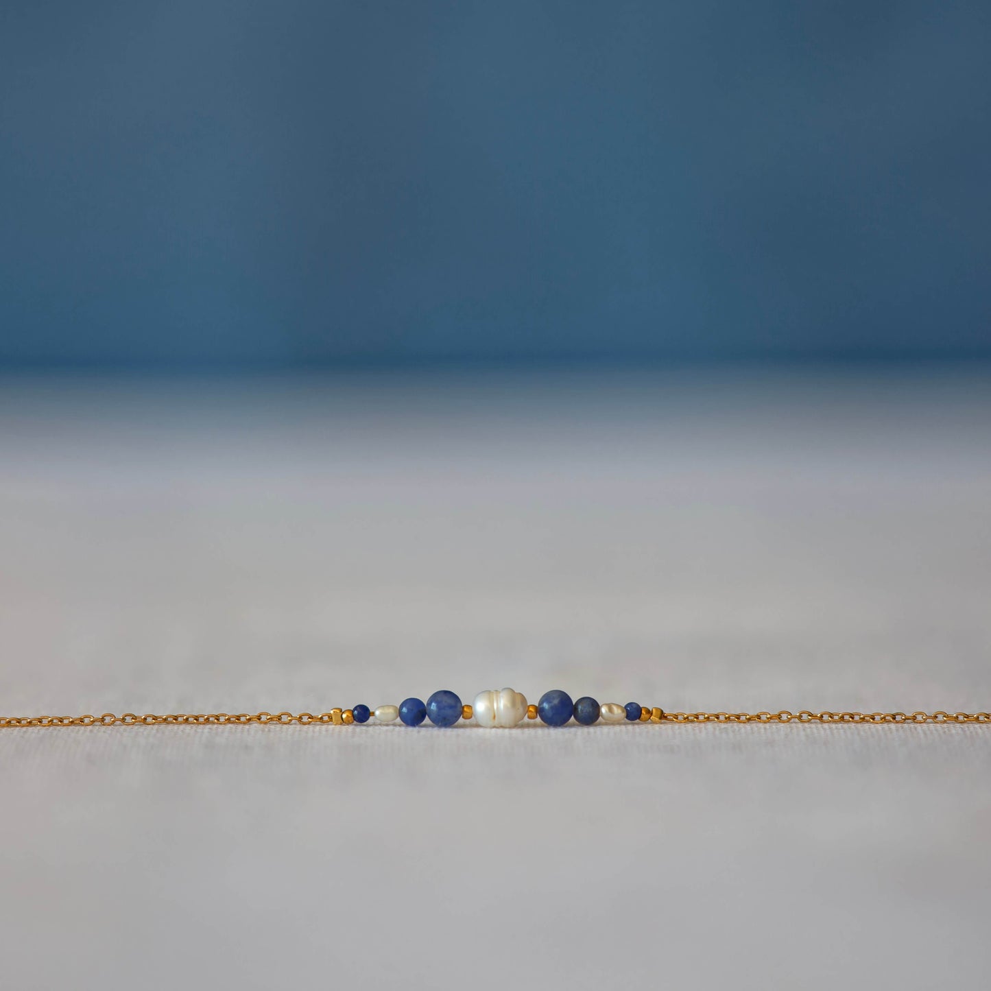 Bracelet Anthelia en perles d'eau douce et perles de sodalite bleue posé sur fond gris.