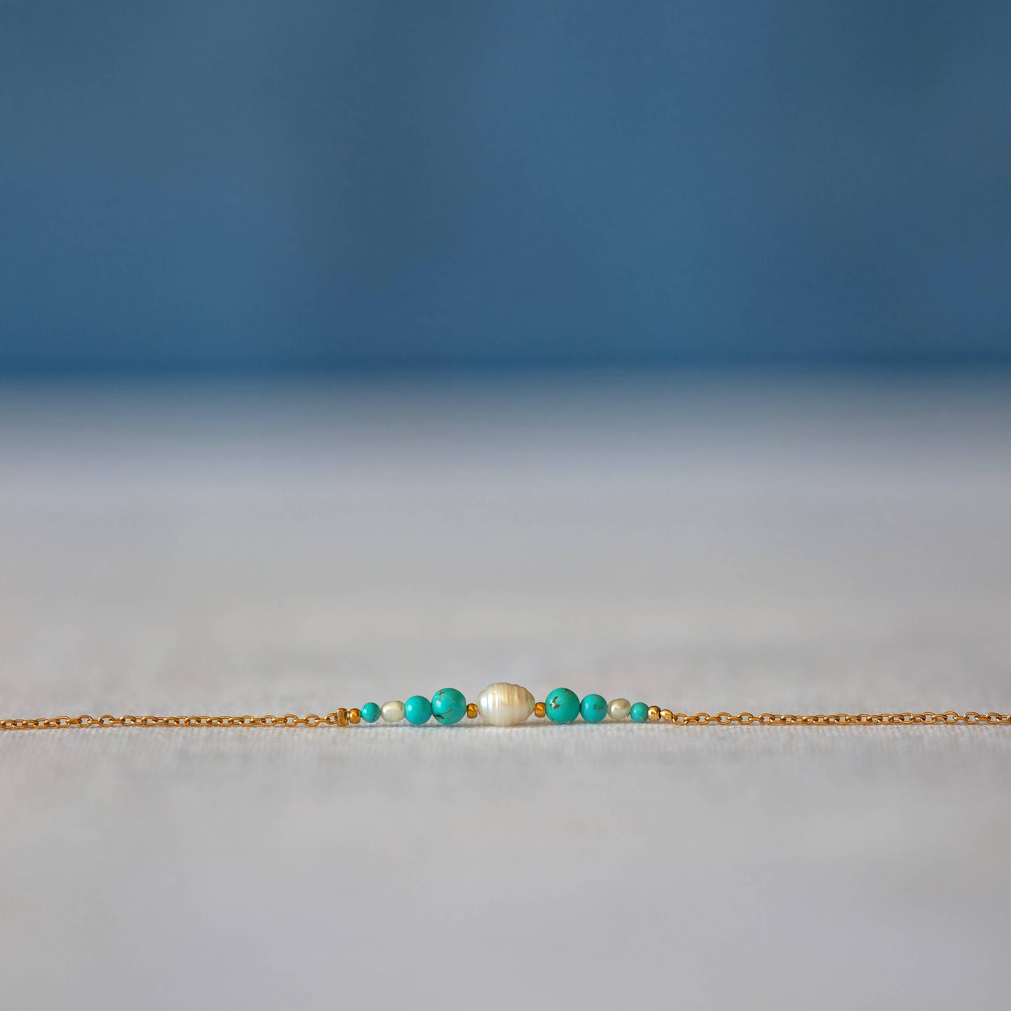 Bracelet Anthelia en perles d'eau douce et perles de turquoise bleue posé sur fond gris.