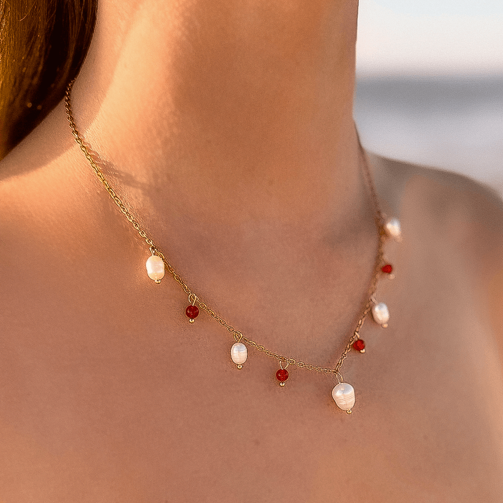 Collier sur chaine en acier inoxydable avec perles d'eau douce et perles de couleur porté par une femme bronzée devant la mer.