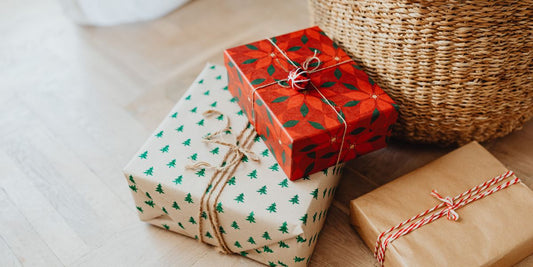 Trois cadeaux de Noël emballés posés sur un parquet à côté d'un panier en osier.