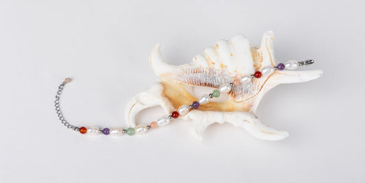 Bracelet en perles d'eau douce et pierres naturelles posé sur un coquillage.