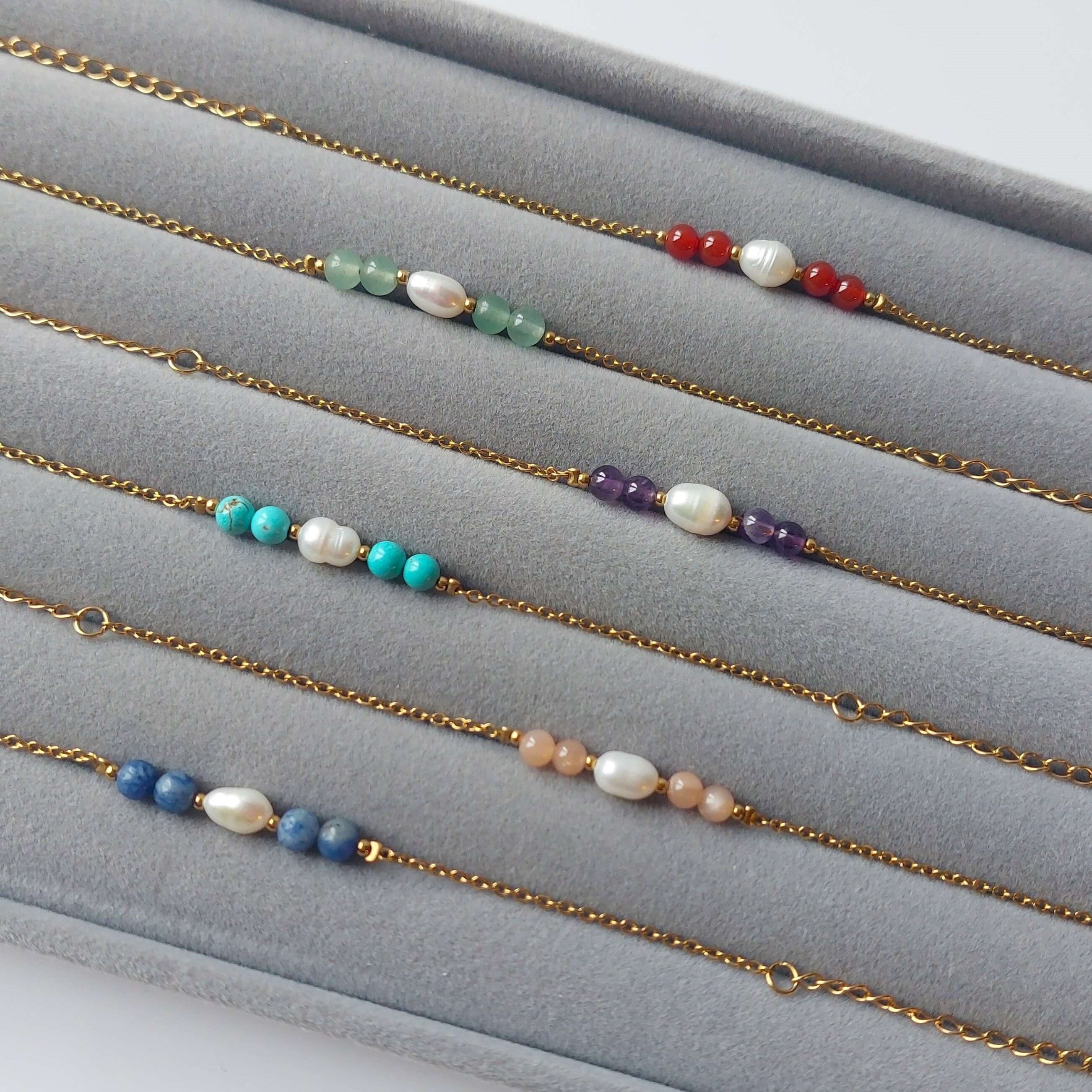 Plateau gris en velours rempli de six bracelets en acier inoxydable doré, perles d'eau duce et pierres de couleur 