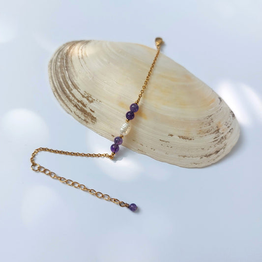 Bracelet élégant Acropora en perle d'eau douce et perles d'améthyste violettes posé sur fond gris.