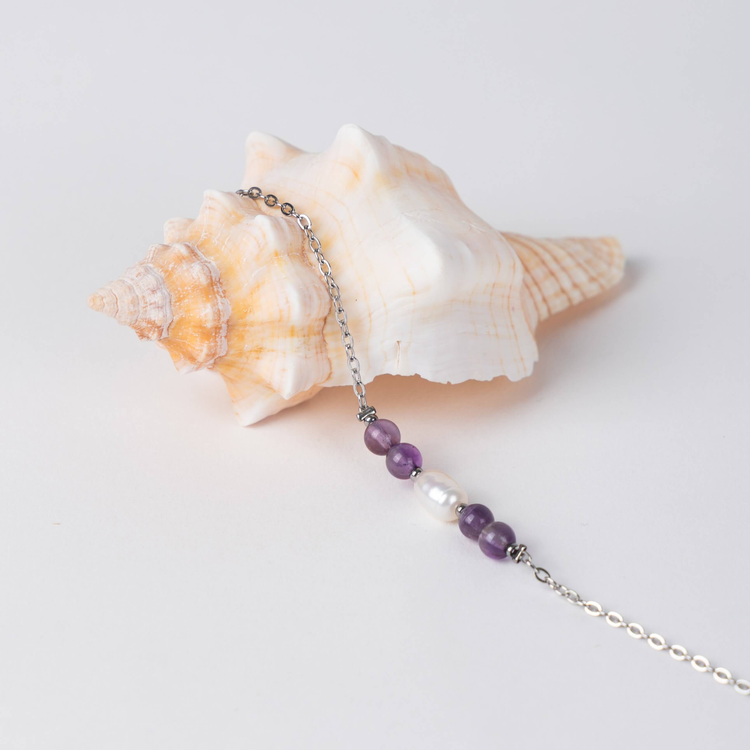 Bracelet en acier inoxydable argenté,perle d'eau douce et perles d'améthyste posé sur fond gris.