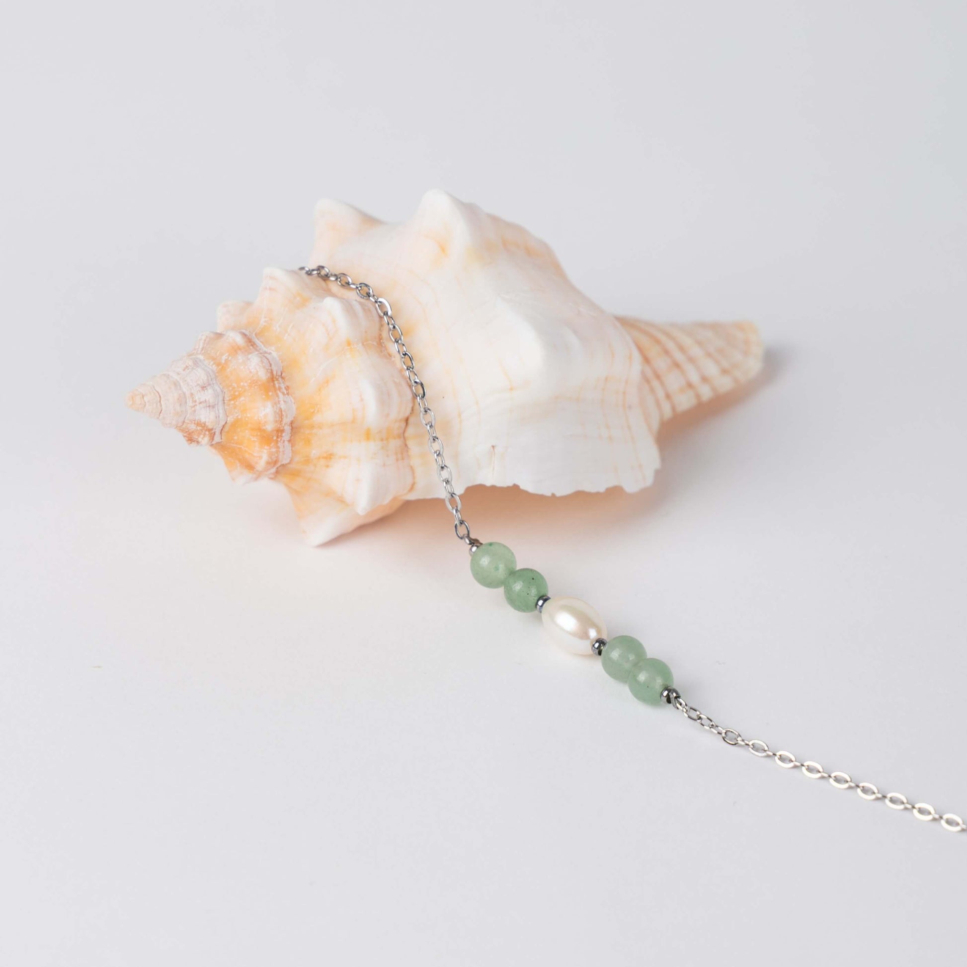 Bracelet en acier inoxydable argenté,perle d'eau douce et perles d'aventurine posé sur fond gris.