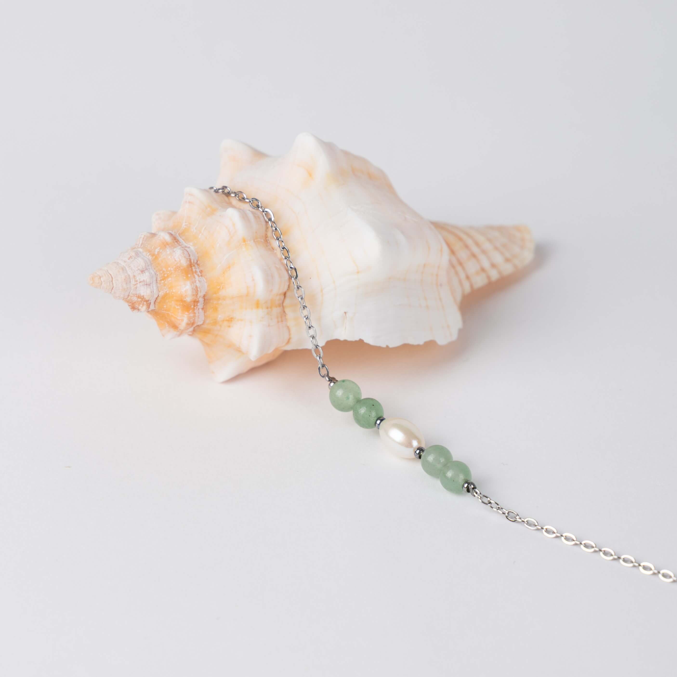 Bracelet en acier inoxydable argenté,perle d'eau douce et perles d'aventurine posé sur fond gris.