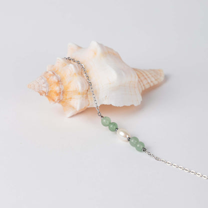 Bracelet en acier inoxydable argenté,perle d'eau douce et perles d'aventurine posé sur fond gris.