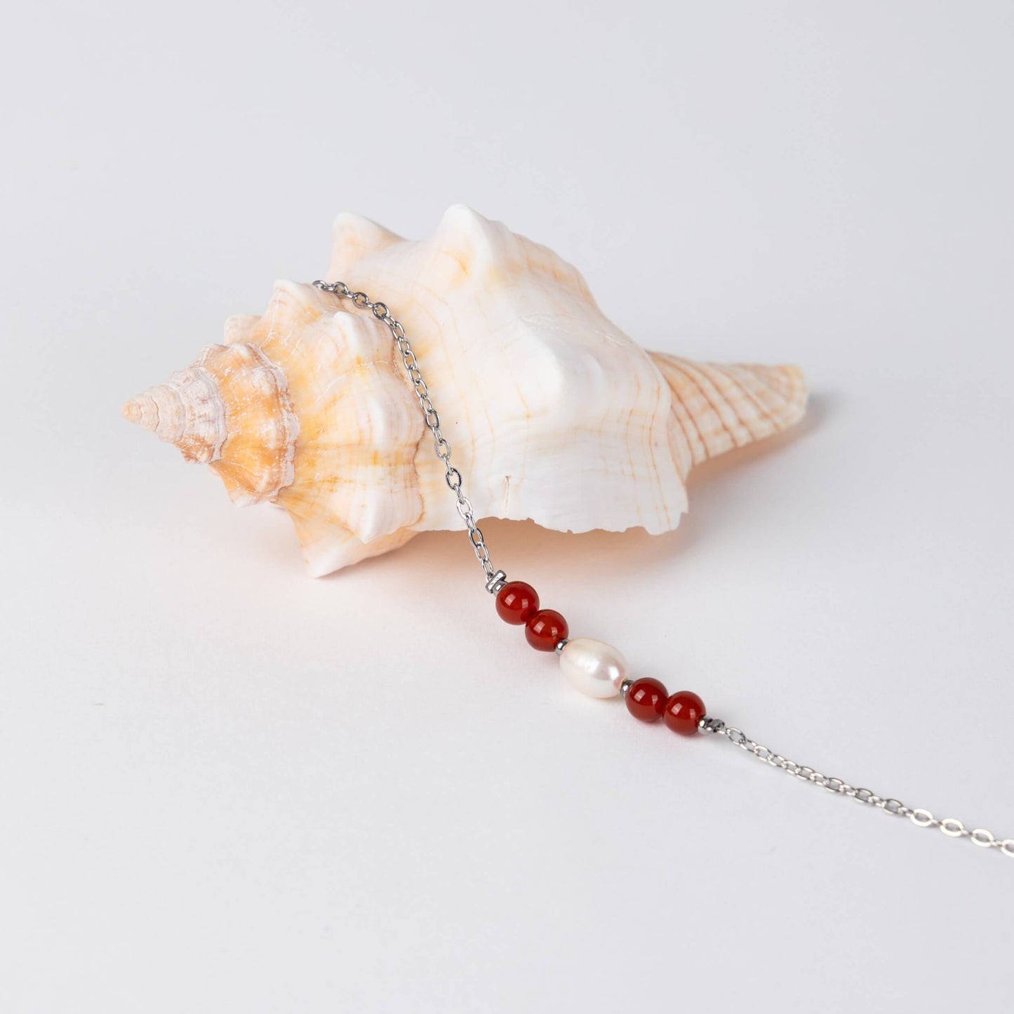 Bracelet en acier inoxydable argenté,perle d'eau douce et perles de cornaline posé sur fond gris.