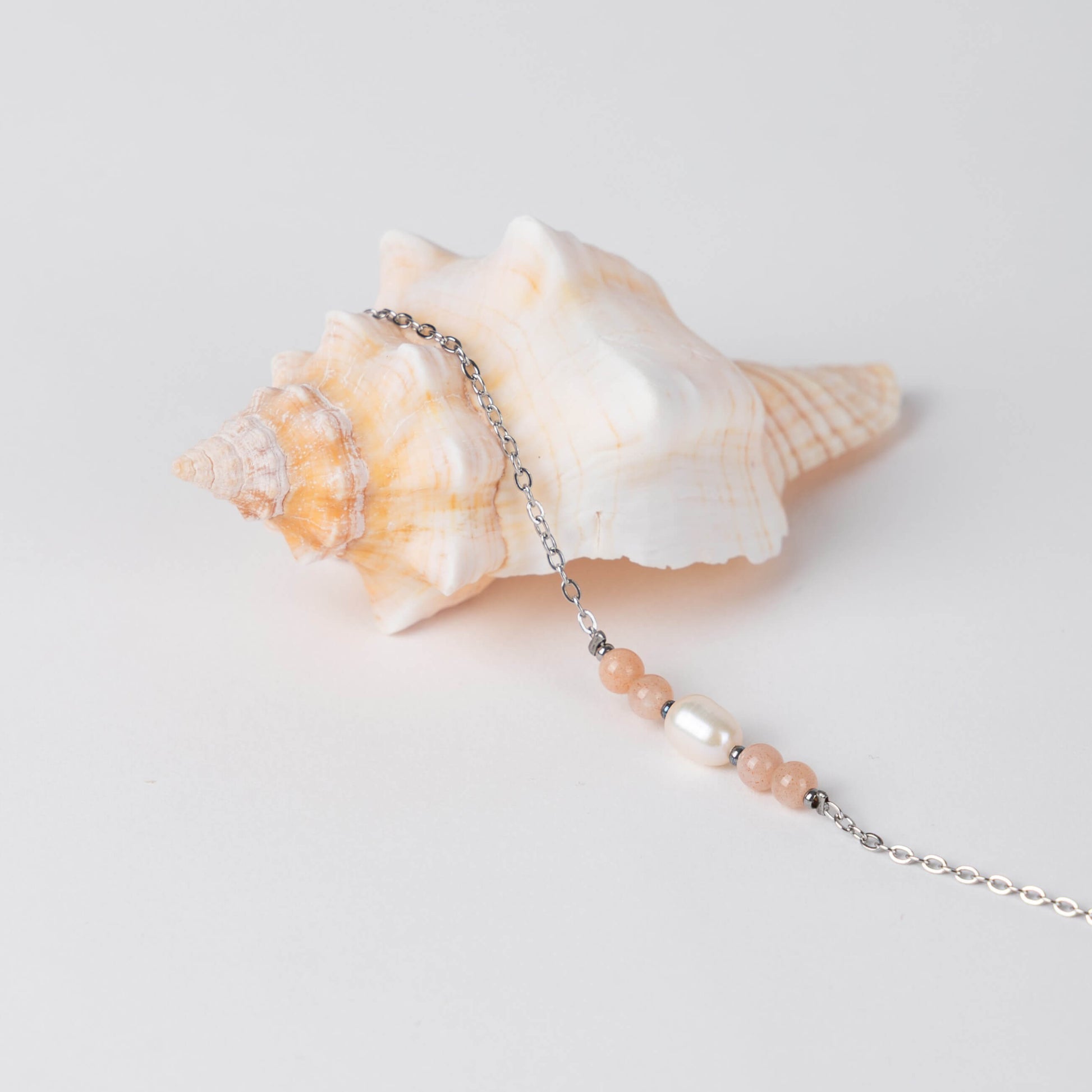 Bracelet en acier inoxydable argenté,perle d'eau douce et perles de pierre de soleil posé sur fond gris.