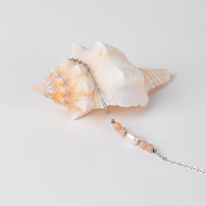 Bracelet en acier inoxydable argenté,perle d'eau douce et perles de pierre de soleil posé sur fond gris.