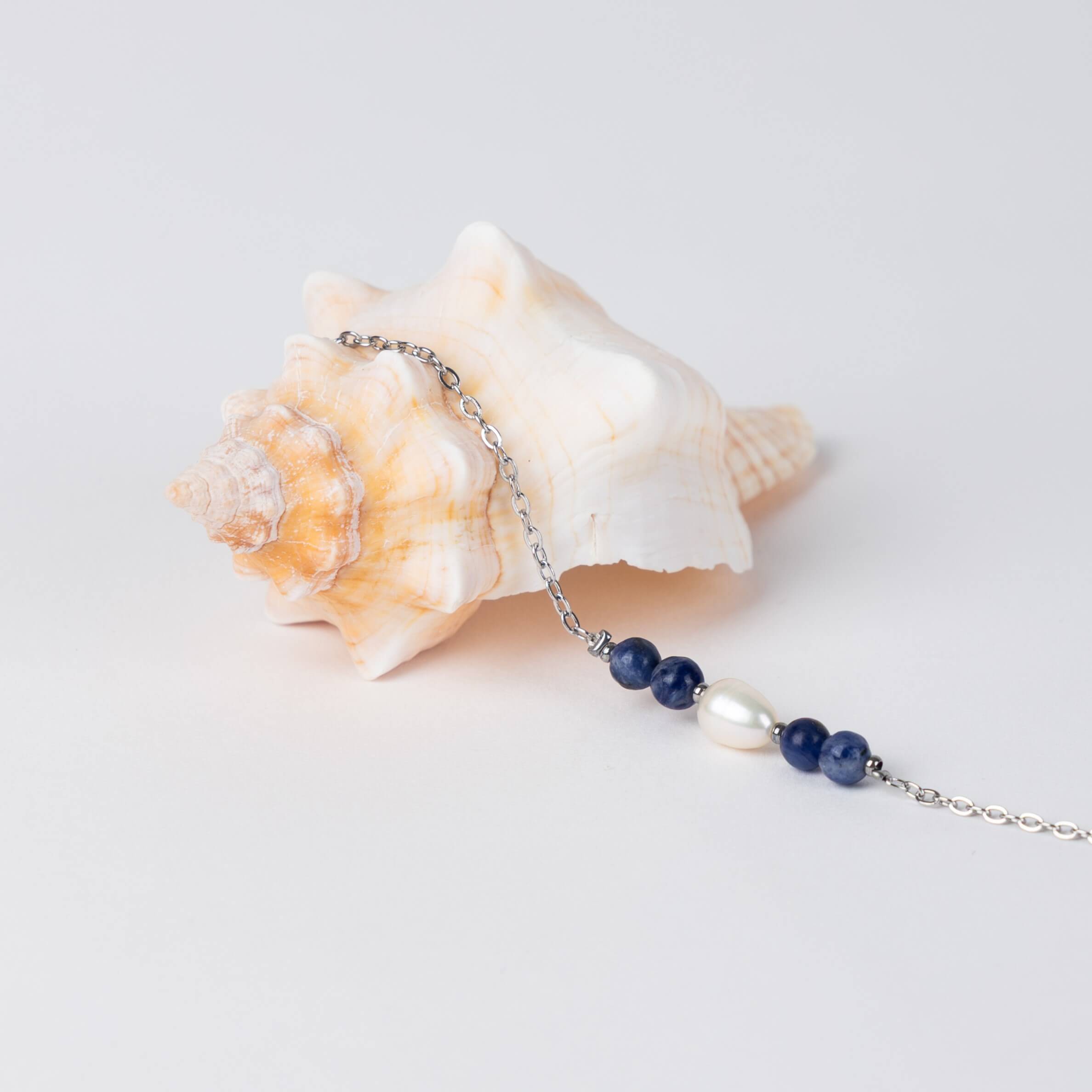 Bracelet en acier inoxydable argenté,perle d'eau douce et perles de sodalite posé sur fond gris.