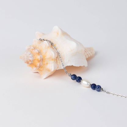 Bracelet en acier inoxydable argenté,perle d'eau douce et perles de sodalite posé sur fond gris.