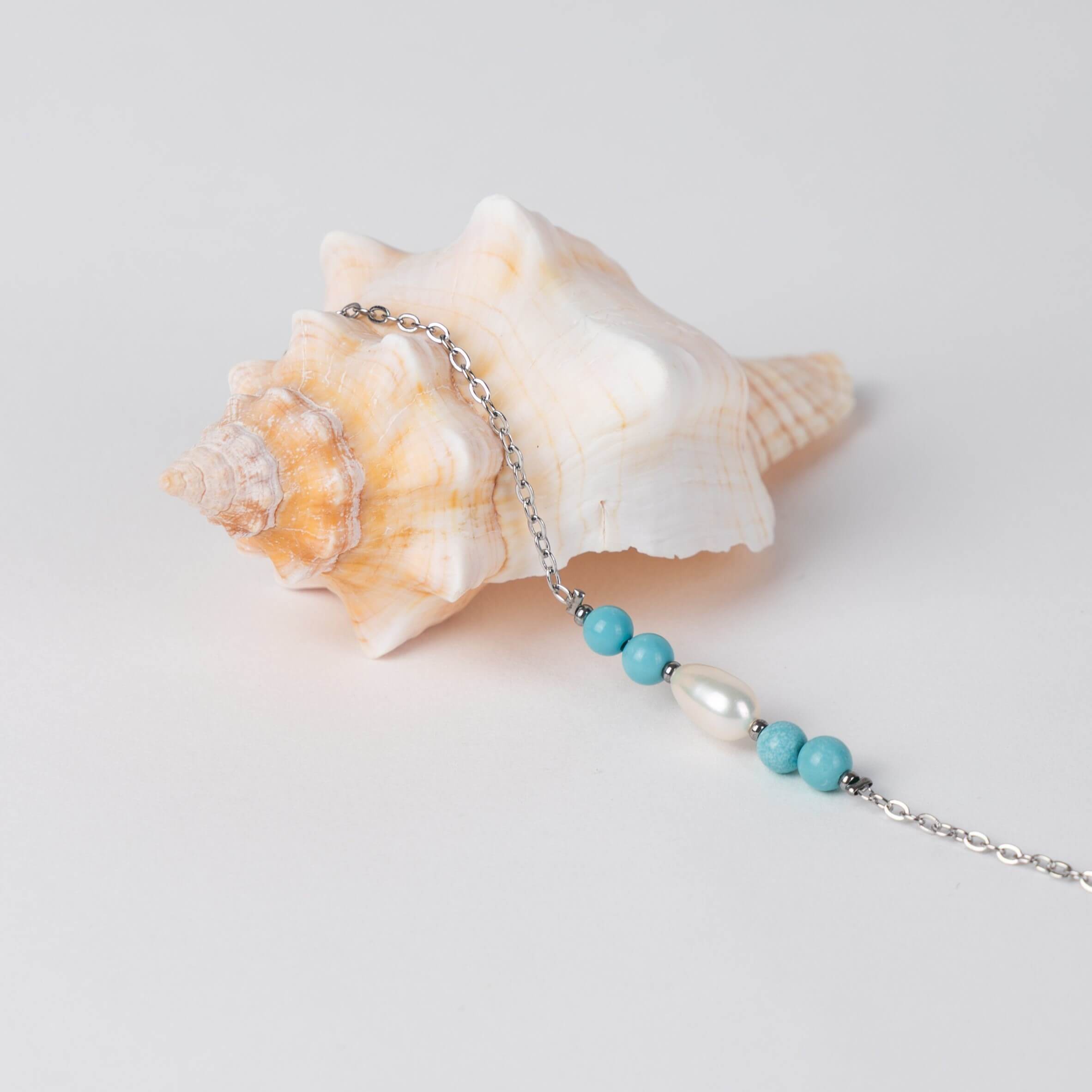 Bracelet en acier inoxydable argenté,perle d'eau douce et perles de turquoise posé sur fond gris.