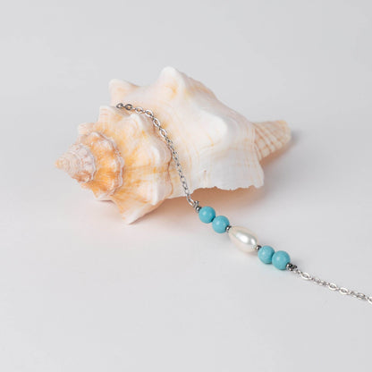 Bracelet en acier inoxydable argenté,perle d'eau douce et perles de turquoise posé sur fond gris.