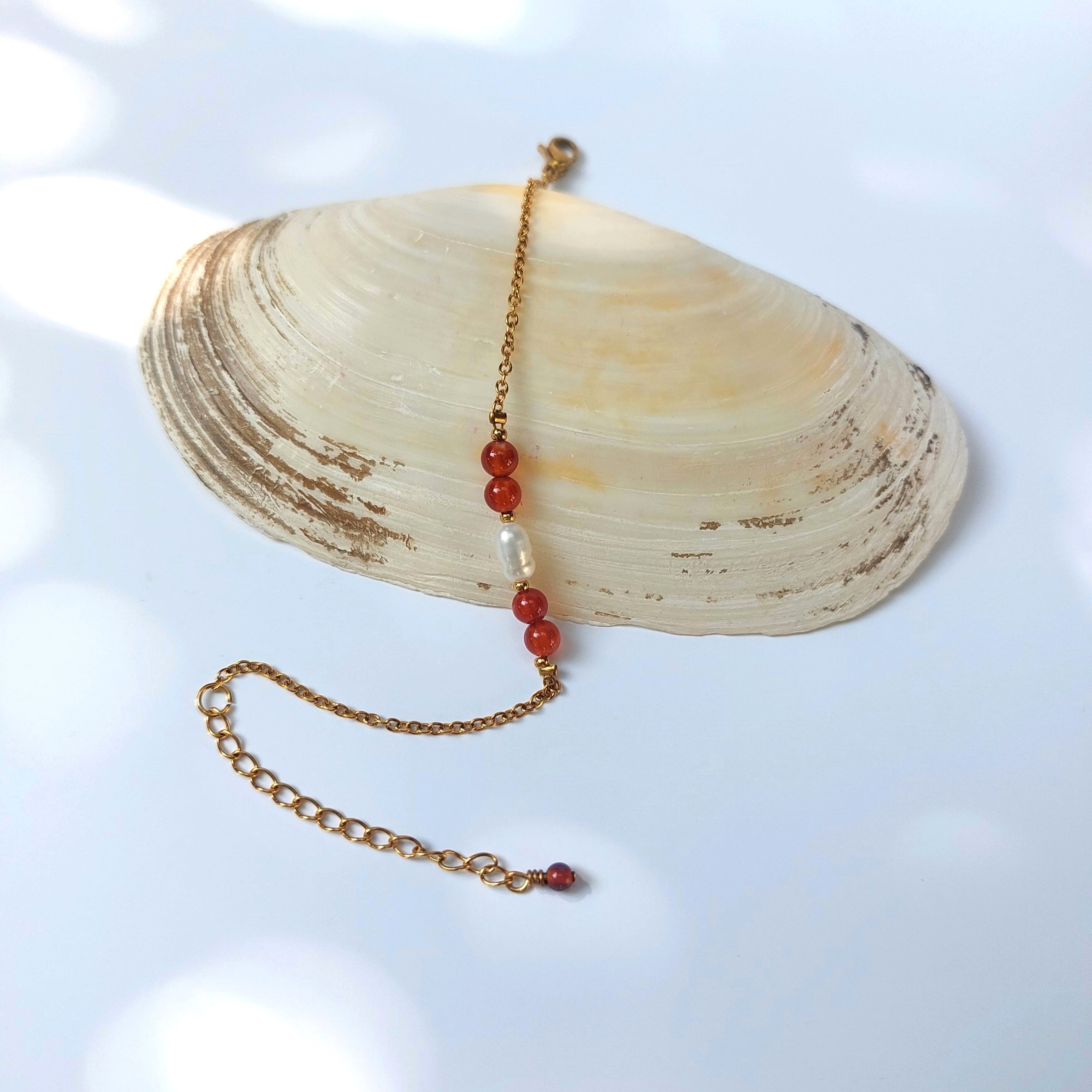 Bracelet élégant Acropora en perle d'eau douce et perles de cornaline orange posé sur fond gris.