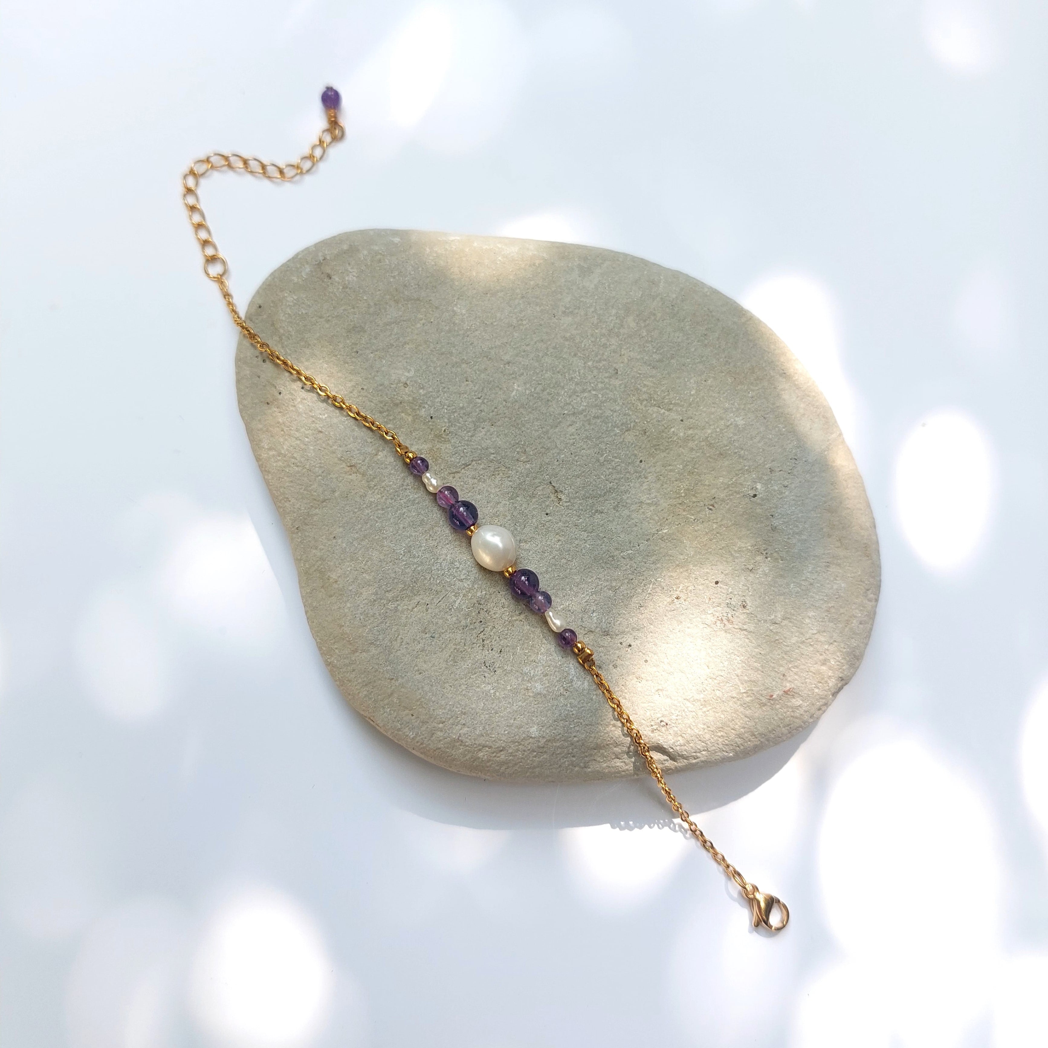 Bracelet Anthelia en perles d'eau douce et perles d'Améthyste violette posé sur fond gris.