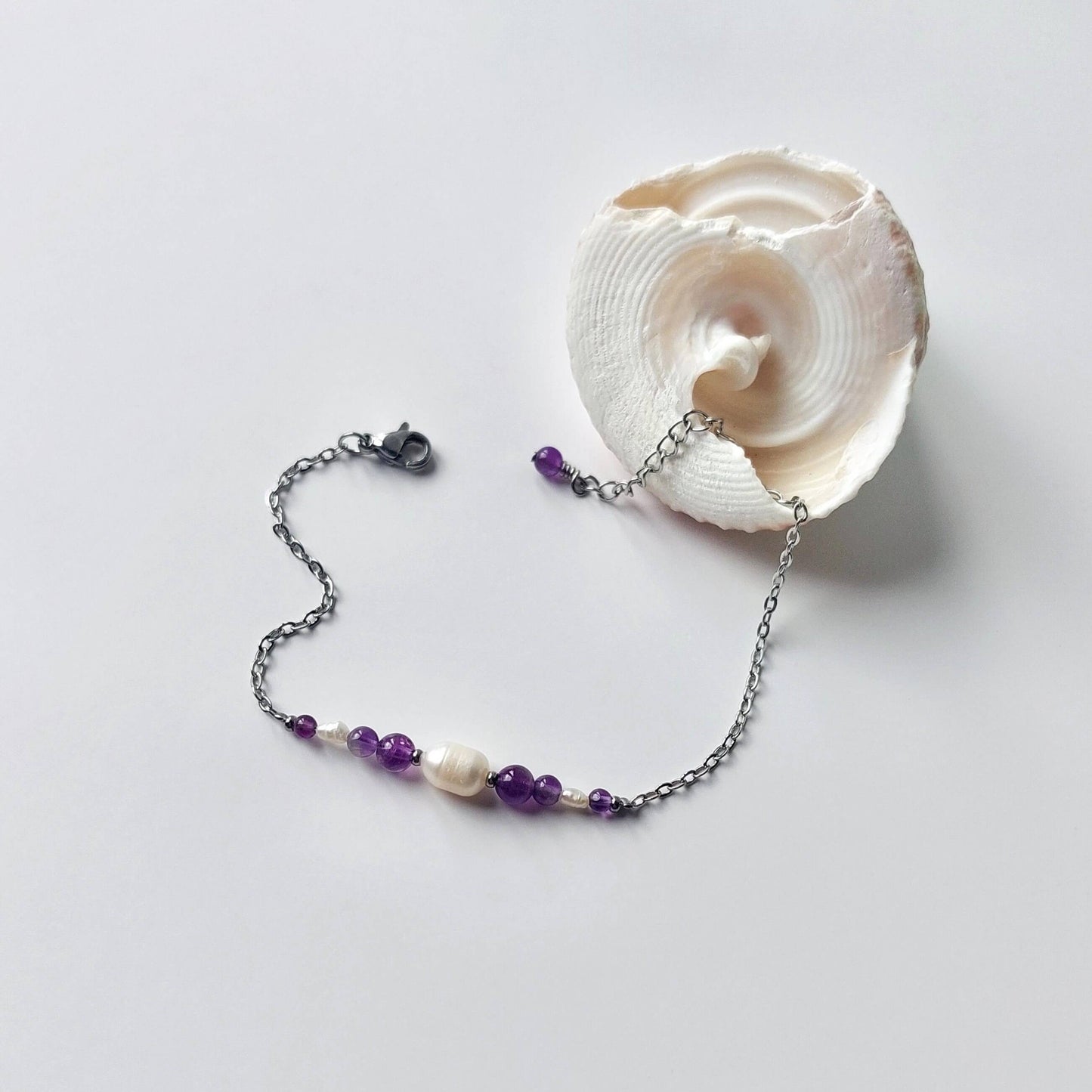 Bracelet en acier inoxydable argenté en perles d'eau douce et perles d'améthyste violette posé sur fond gris.