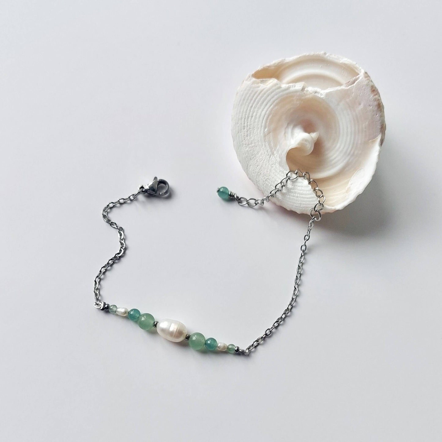 Bracelet en acier inoxydable argenté en perles d'eau douce et perles d'aventurine verte posé sur fond gris.