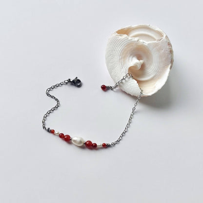 Bracelet en acier inoxydable argenté en perles d'eau douce et perles de cornaline rouge posé sur fond gris.