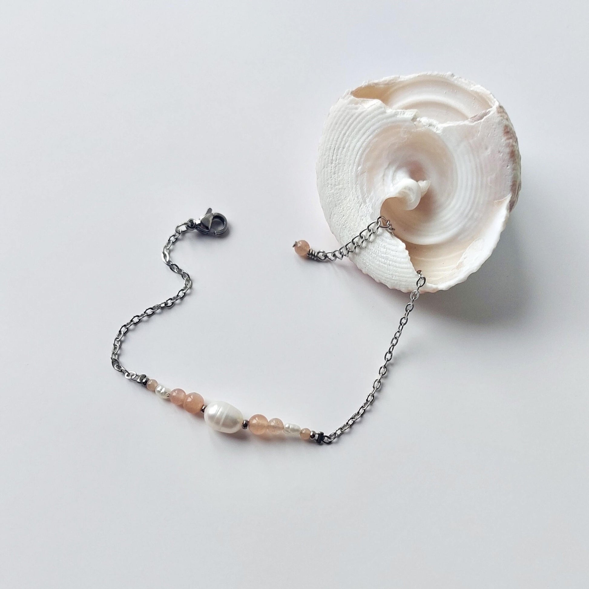 Bracelet en acier inoxydable argenté en perles d'eau douce et perles de pierre de soleil rose posé sur fond gris.