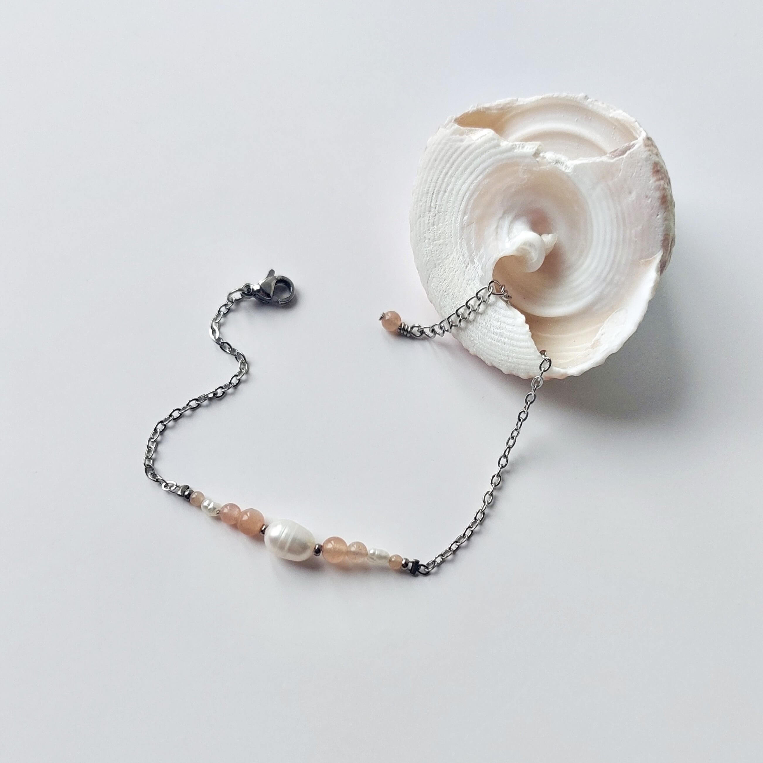 Bracelet en acier inoxydable argenté en perles d'eau douce et perles de pierre de soleil rose posé sur fond gris.