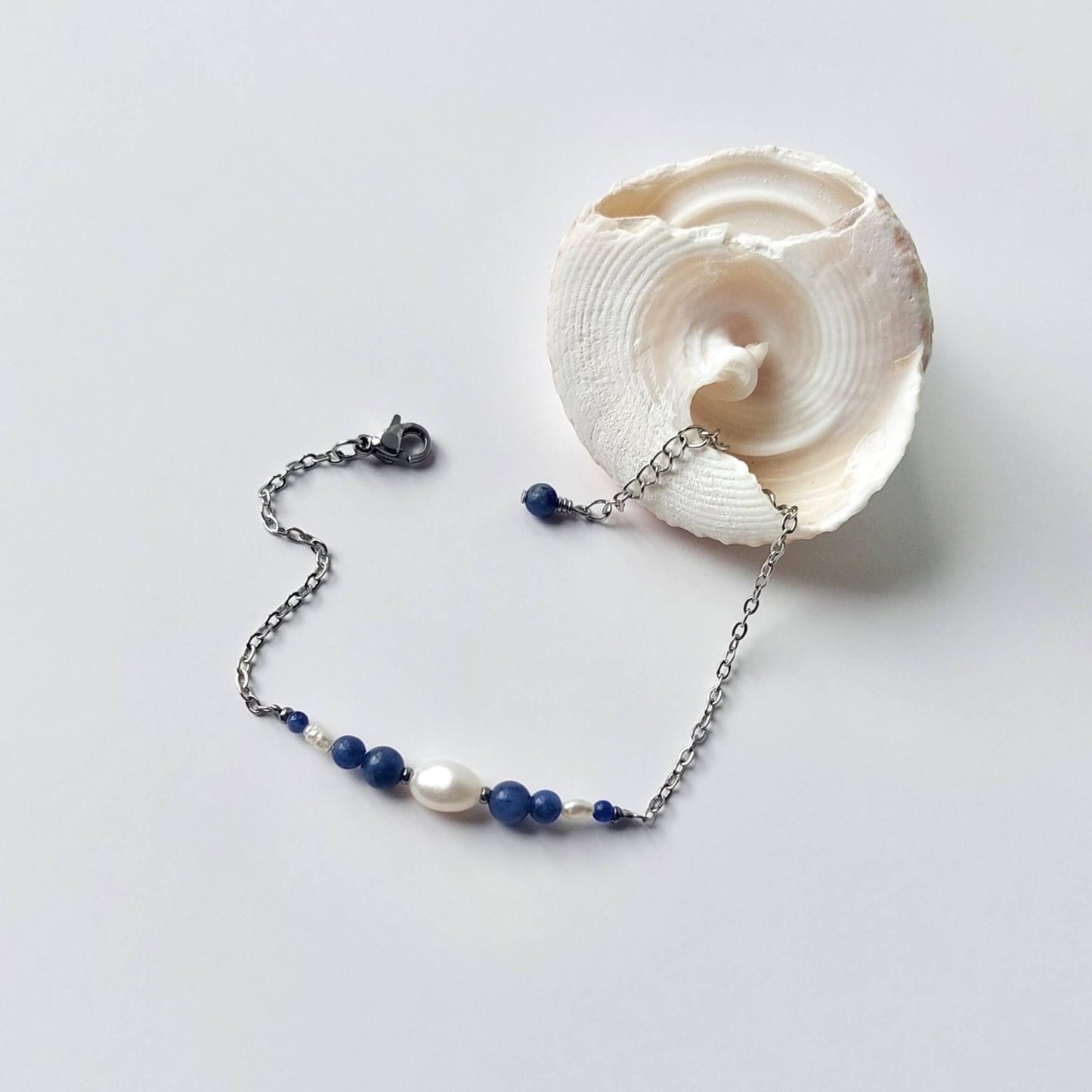 Bracelet en acier inoxydable argenté en perles d'eau douce et perles de sodalite bleue posé sur fond gris.