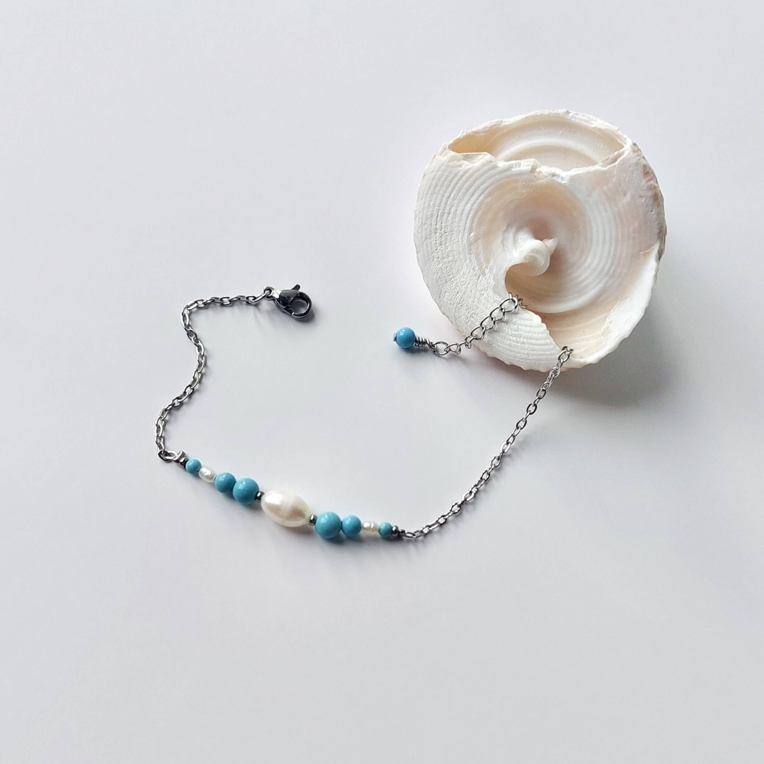 Bracelet en acier inoxydable argenté en perles d'eau douce et perles de turquoise bleue posé sur fond gris.
