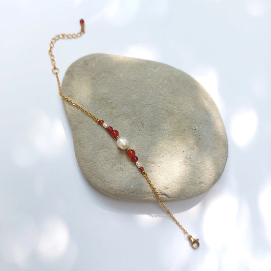 Bracelet Anthelia en perles d'eau douce et perles de cornaline rouge posé sur fond gris.