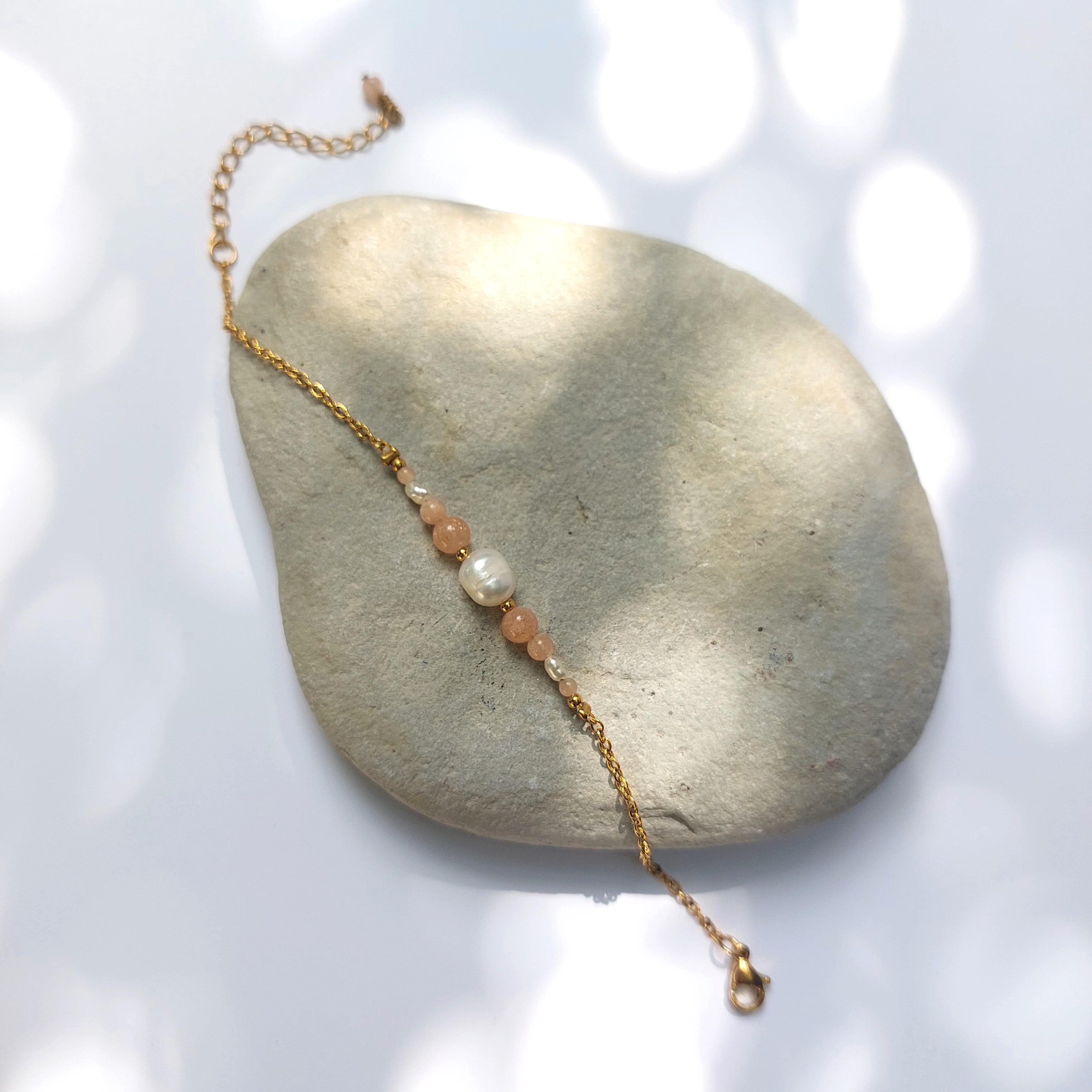 Bracelet Anthelia en perles d'eau douce et perles de pierre de soleil rose posé sur fond gris.