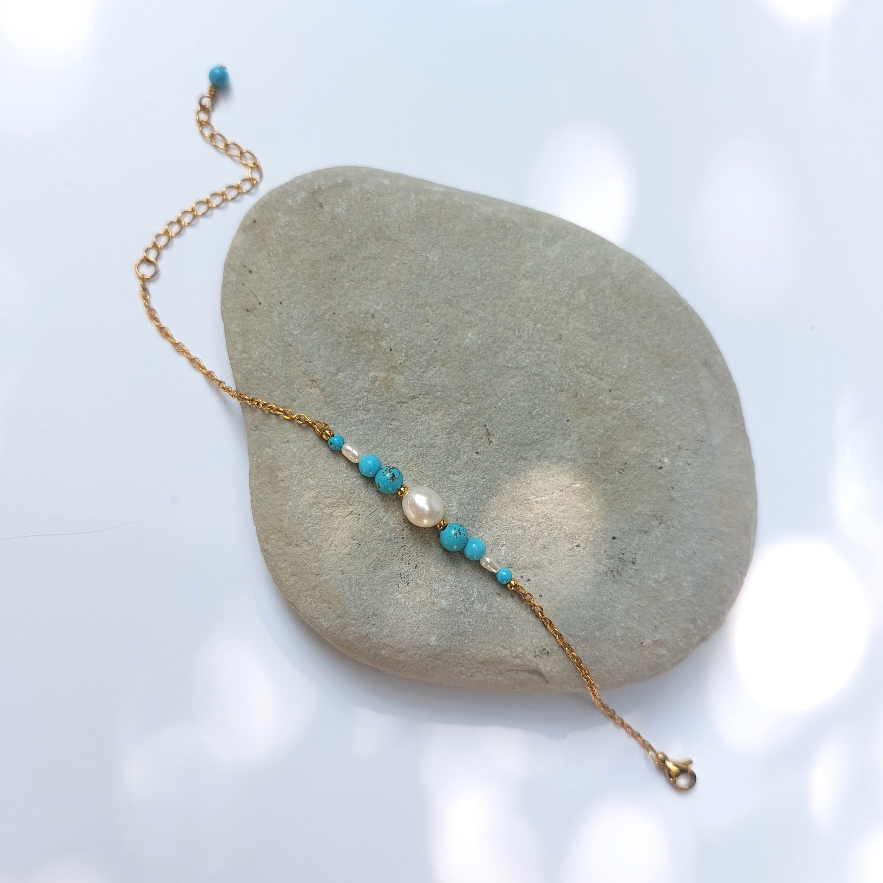 Bracelet Anthelia en perles d'eau douce et perles de turquoise bleue posé sur fond gris.