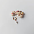 Paire de boucles d'oreilles Favia en créoles dorées en acier inoxydable avec une pierre de quartz fraise rose et une perle d'eau douce baroque en pendentif, posées sur un morceau de corail blanc tacheté de rose sur fond gris clair.