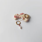 Paire de boucles d'oreilles Favia en créoles dorées en acier inoxydable avec une pierre de quartz fraise rose et une perle d'eau douce baroque en pendentif, posées sur un morceau de corail blanc tacheté de rose sur fond gris clair.