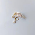 Boucles d’oreilles créoles en acier inoxydable doré avec perles d’eau douce naturelles blanches, posées sur un coquillage, style élégant, sur fond neutre.