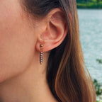Boucles d'oreilles pendantes avec petites perles d'eau douce violette irrégulières, sur un fond d'eau flouté. 