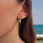 Boucles d'oreilles pendantes en trio de petites perles d'eau douce blanche porté par une femme à la plage