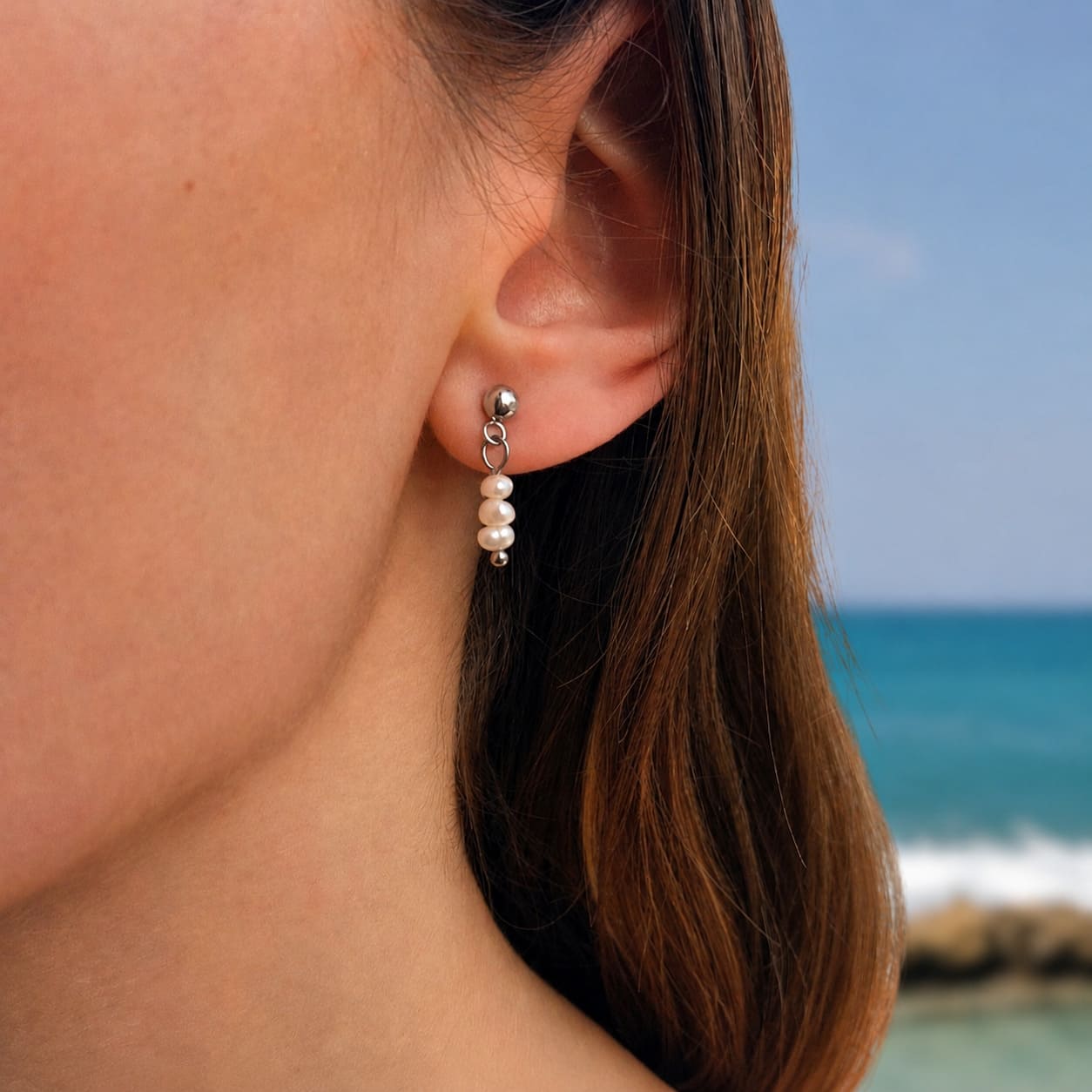 Boucles d'oreilles pendantes en trio de petites perles d'eau douce blanche porté par une femme à la plage