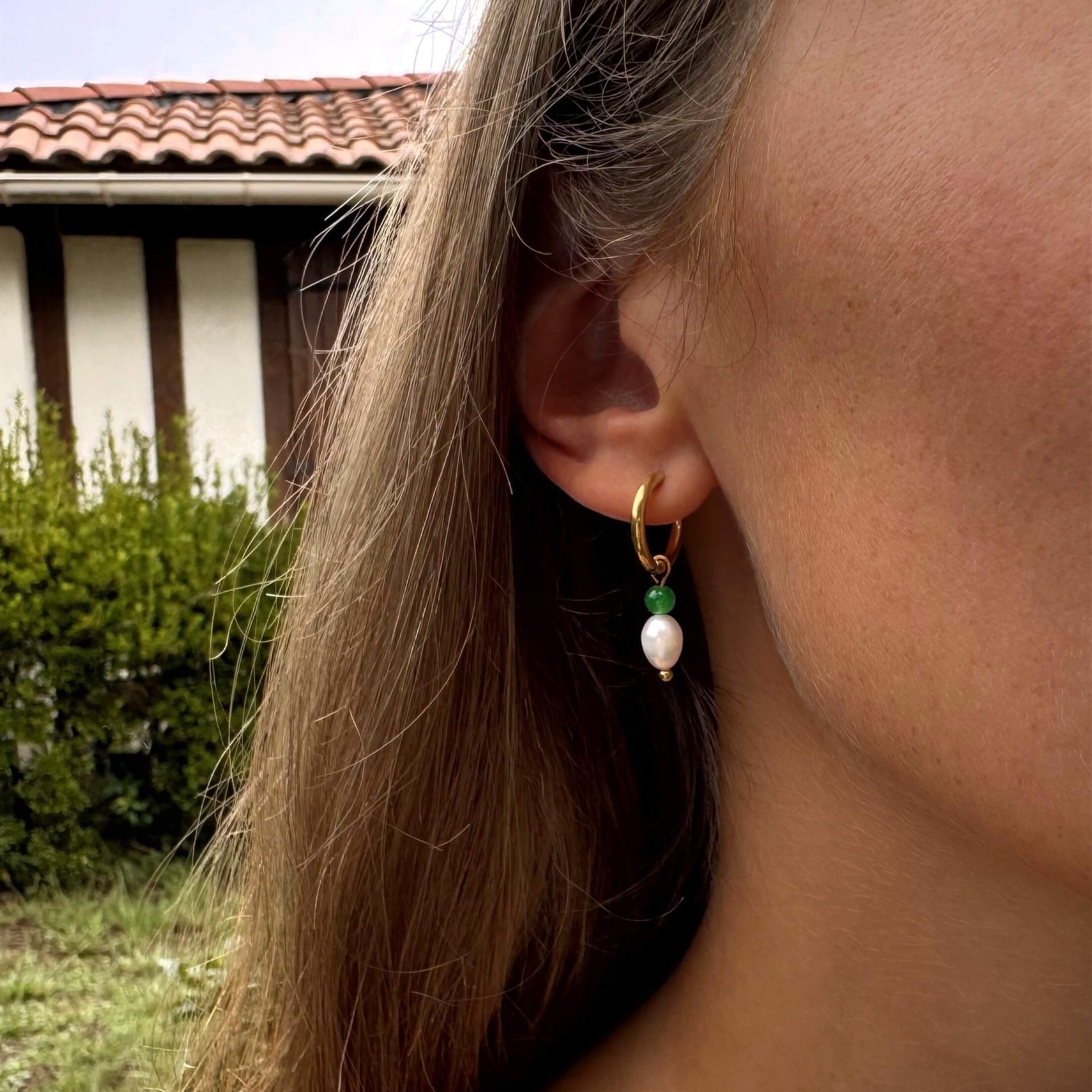 Boucles d'oreilles créoles en acier inoxydable perles d'eau duce et pierres d'aventurine verte portées par une femme