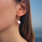 Boucles d'oreilles créoles portées avec perle d'eau douce plate violette pendantes. 