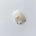 Bague élastique faite uniquement de petites perles d'eau douce blanches posée sur un coquillage