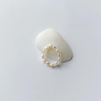 Bague élastique faite uniquement de petites perles d'eau douce blanches posée sur un coquillage