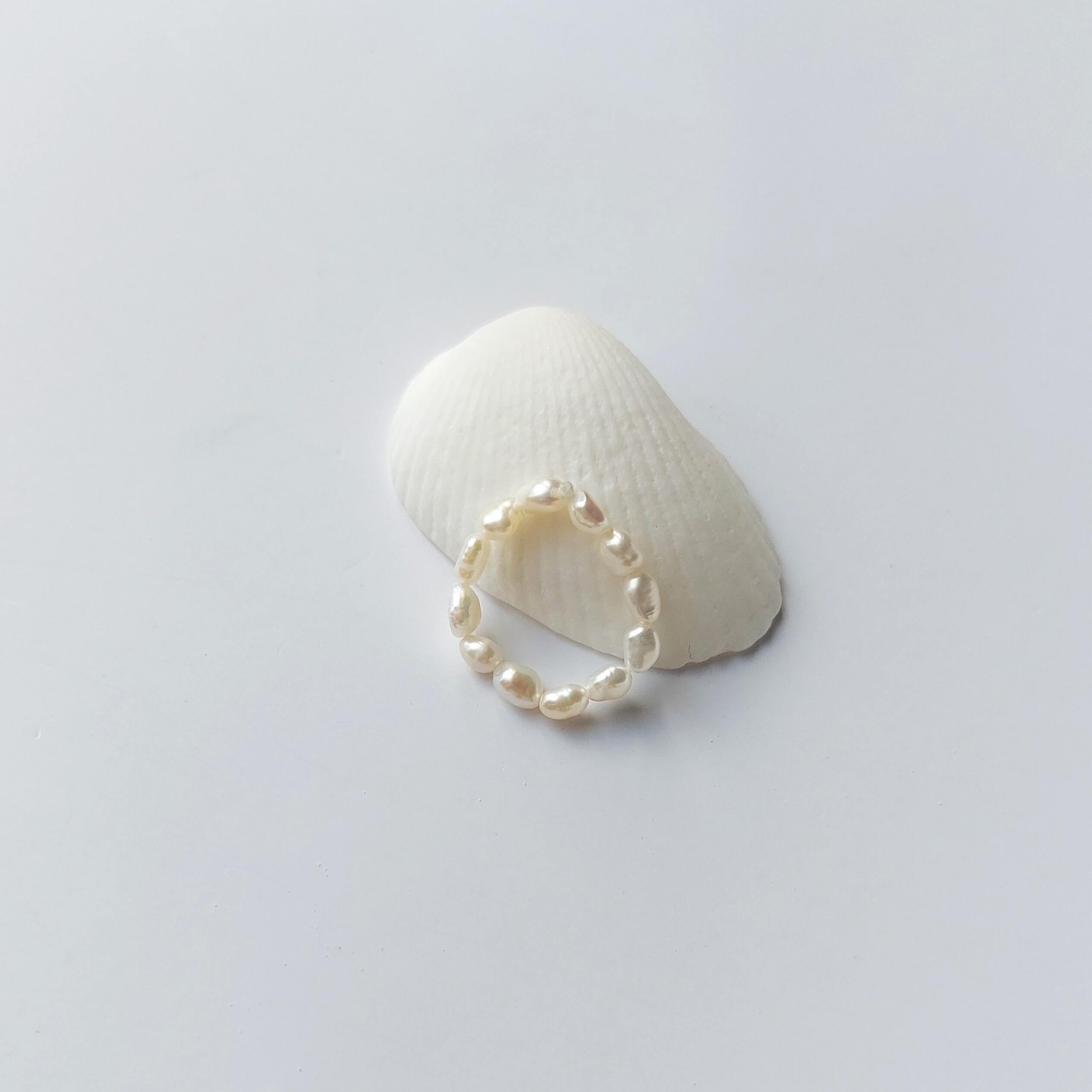 Bague élastique faite uniquement de petites perles d'eau douce blanches posée sur un coquillage