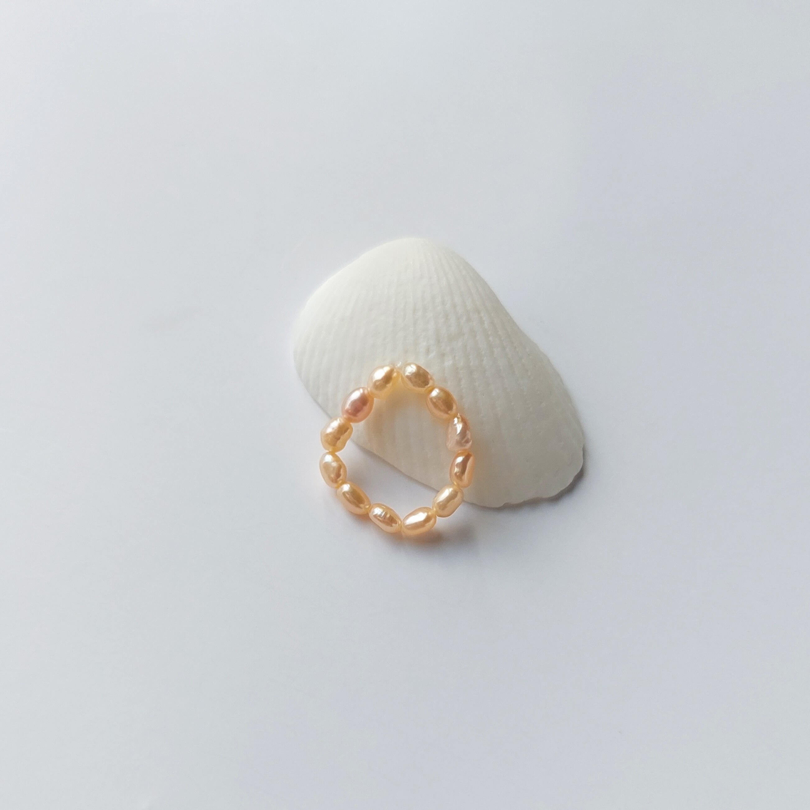 Bague élastique faite uniquement de petites perles d'eau douce oranges posée sur un coquillage