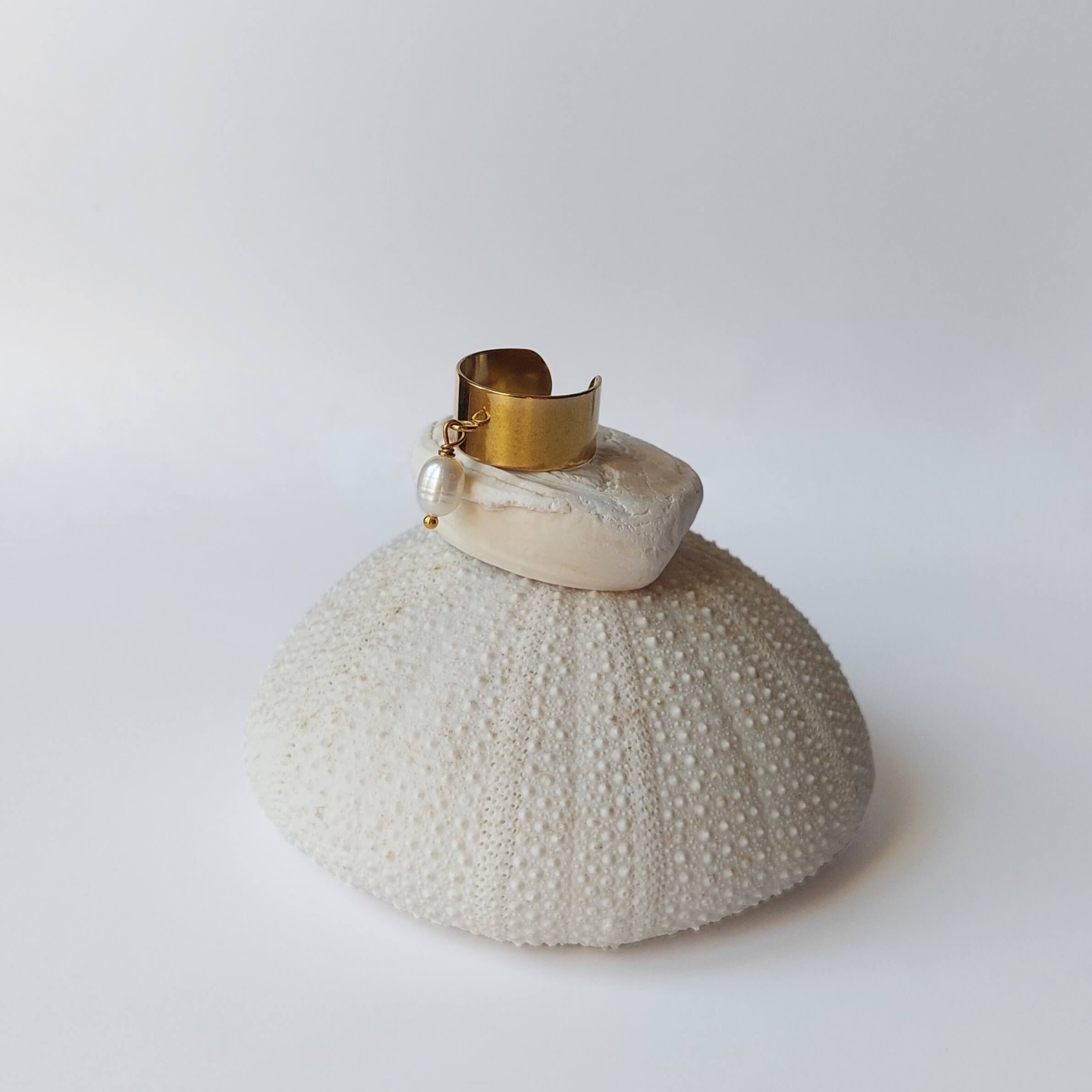 Bague en acier inoxydable doré avec breloque perle d'eau douce blanche posée sur un coquillage