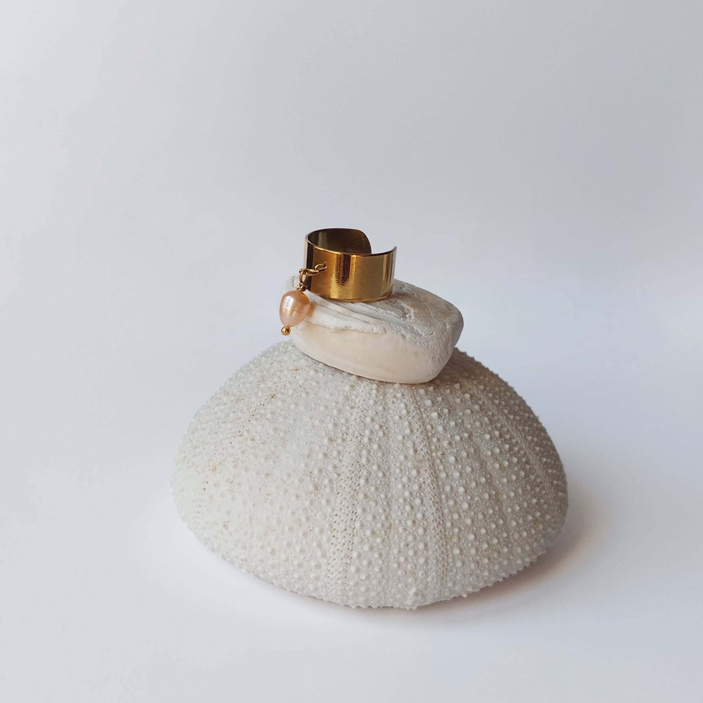 Bague en acier inoxydable doré avec breloque perle d'eau douce orange posée sur un coquillage