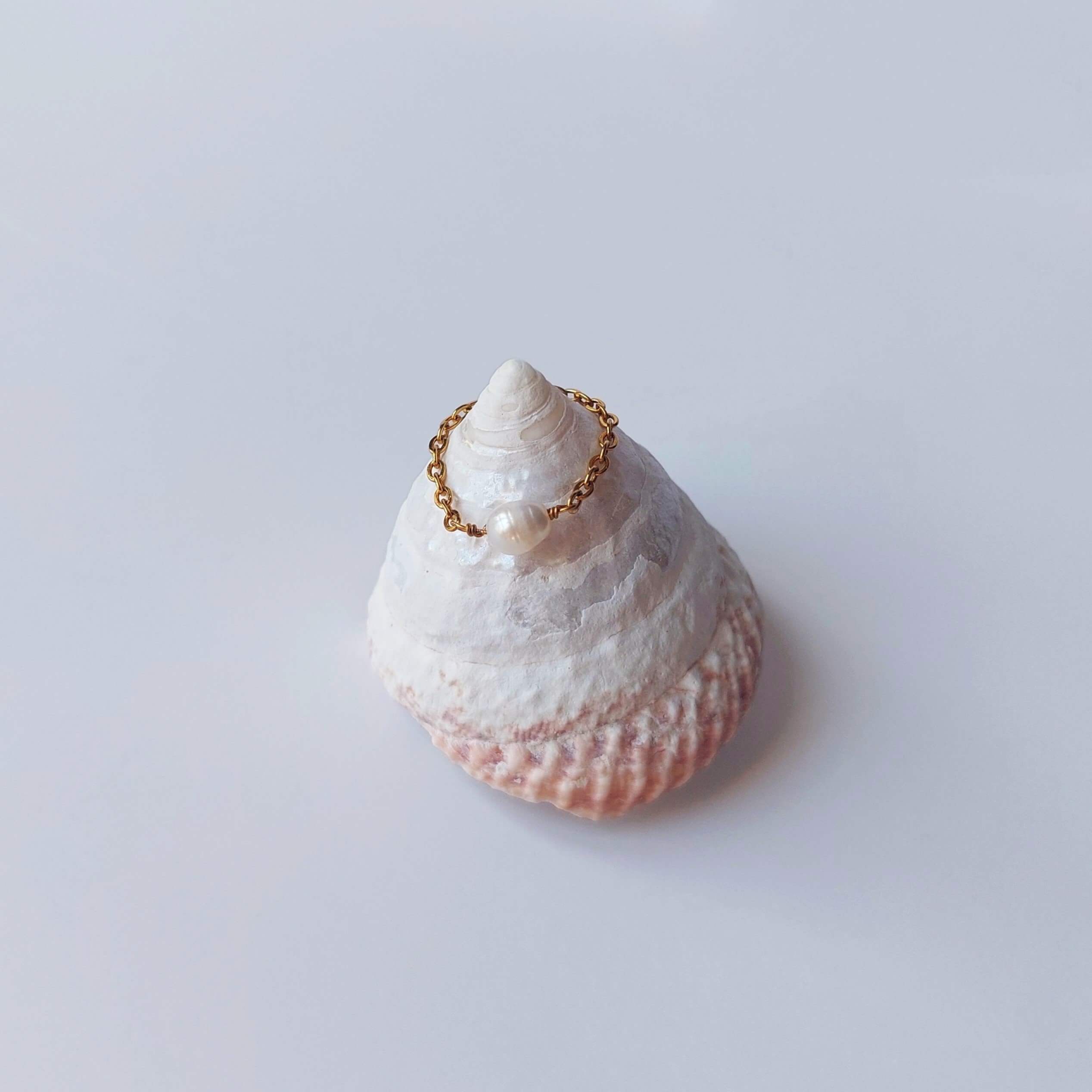 Bague faite d'une chaine fine en acier inoxydable doré et perle d'eau douce blanche posée sur un coquillage